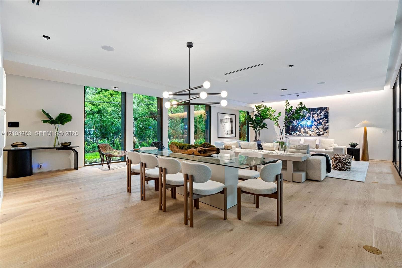 Open-concept living space featuring wood-finish flooring, floor-to-ceiling windows, recessed lighting, and a modern tiered geometric chandelier