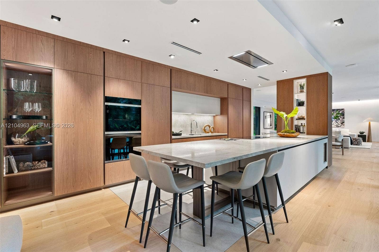 Kitchen featuring flat-panel wood cabinetry, integrated stainless steel double wall ovens, a stone-topped island with waterfall edge, and wood-finish flooring