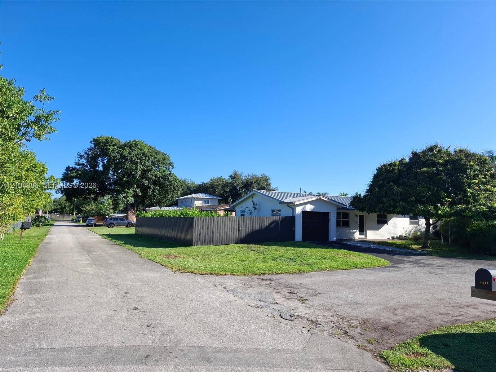 Davie, FL 33314 Single-story exterior featuring a metal roof, an attached garage, and a fenced-in side yard situated on a corner lot with paved driveway access