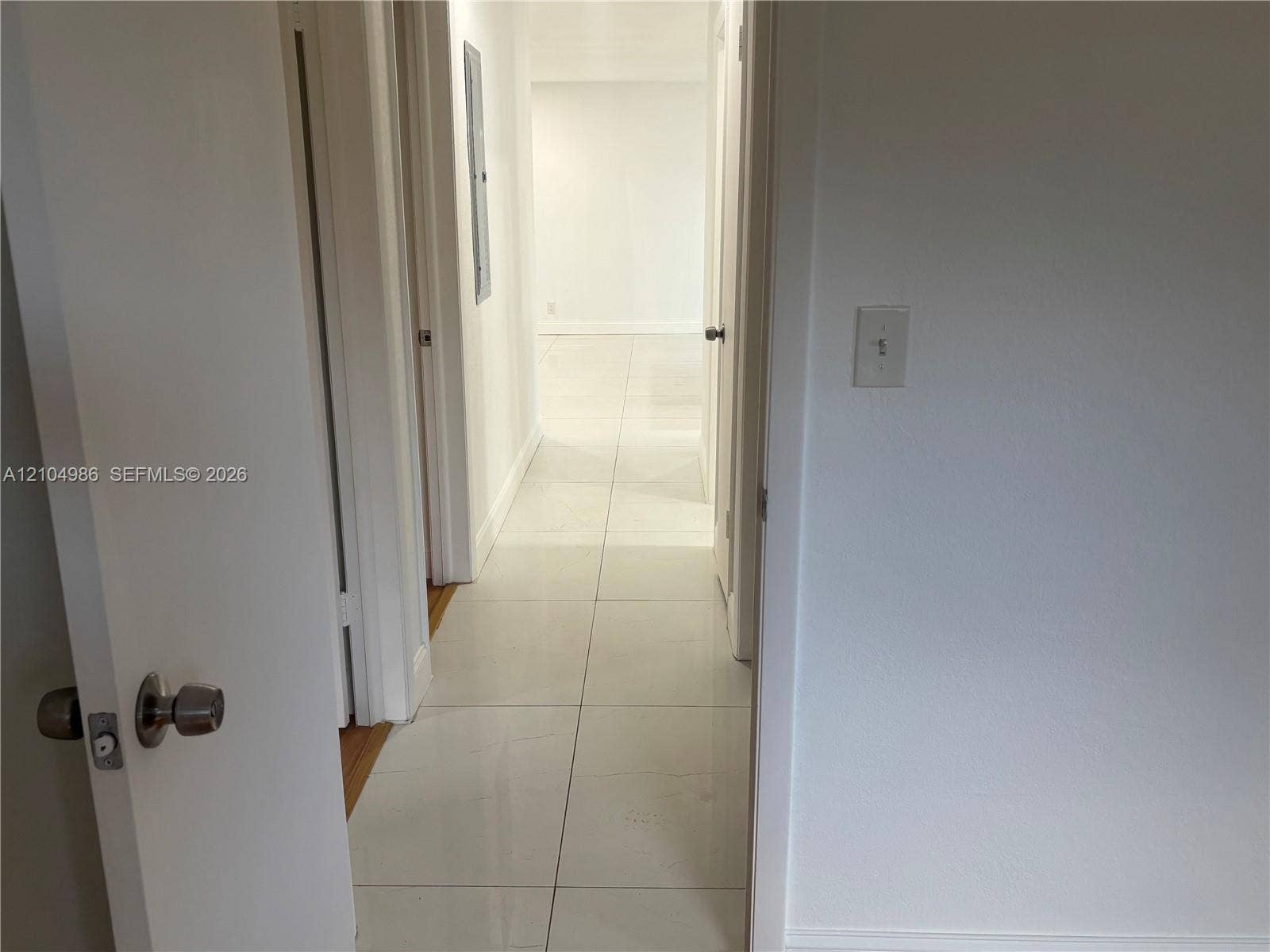 Davie, FL 33314 Interior hallway featuring large-format ceramic tile flooring, neutral wall finishes, and solid-core interior doors with satin nickel hardware