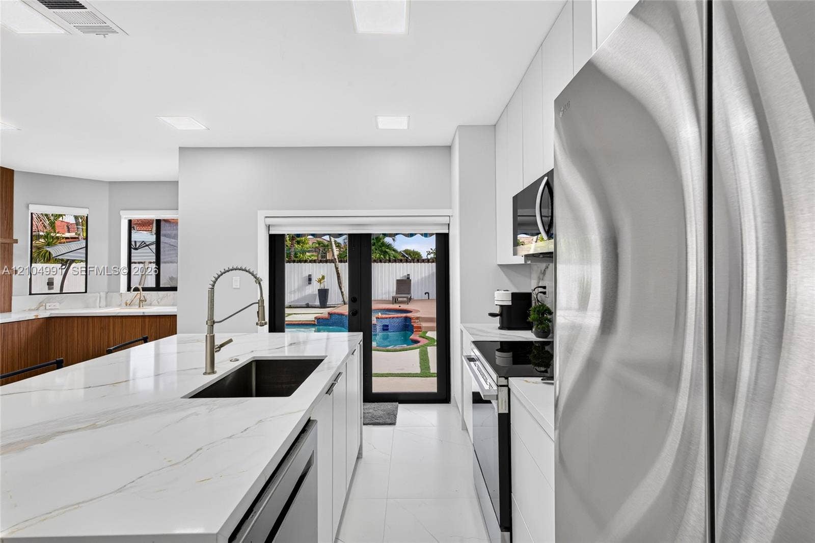 15217 SW 36th Terrace, #0, Miami, Miami, FL 33185 Kitchen featuring a central island with a stone-finish countertop and undermount sink, stainless steel appliances, flat-panel cabinetry, and black-framed double doors