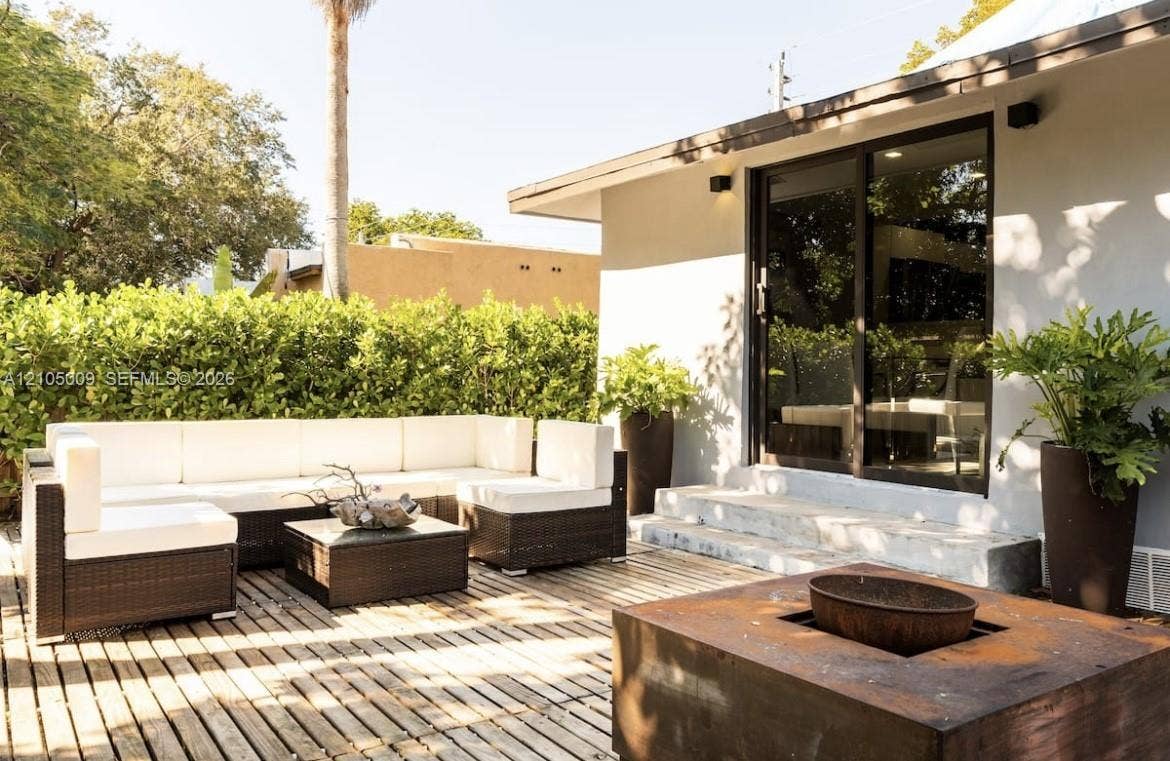 254 NW 51st Street, Miami, Miami, FL 33127 Exterior wood deck with a built-in fire pit, privacy hedging, concrete steps, and dark-framed sliding glass doors