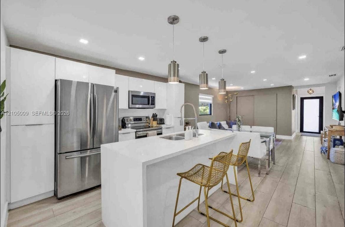 254 NW 51st Street, Miami, Miami, FL 33127 Modern kitchen featuring white cabinetry, stainless steel appliances, a center island with sink, and pendant lighting