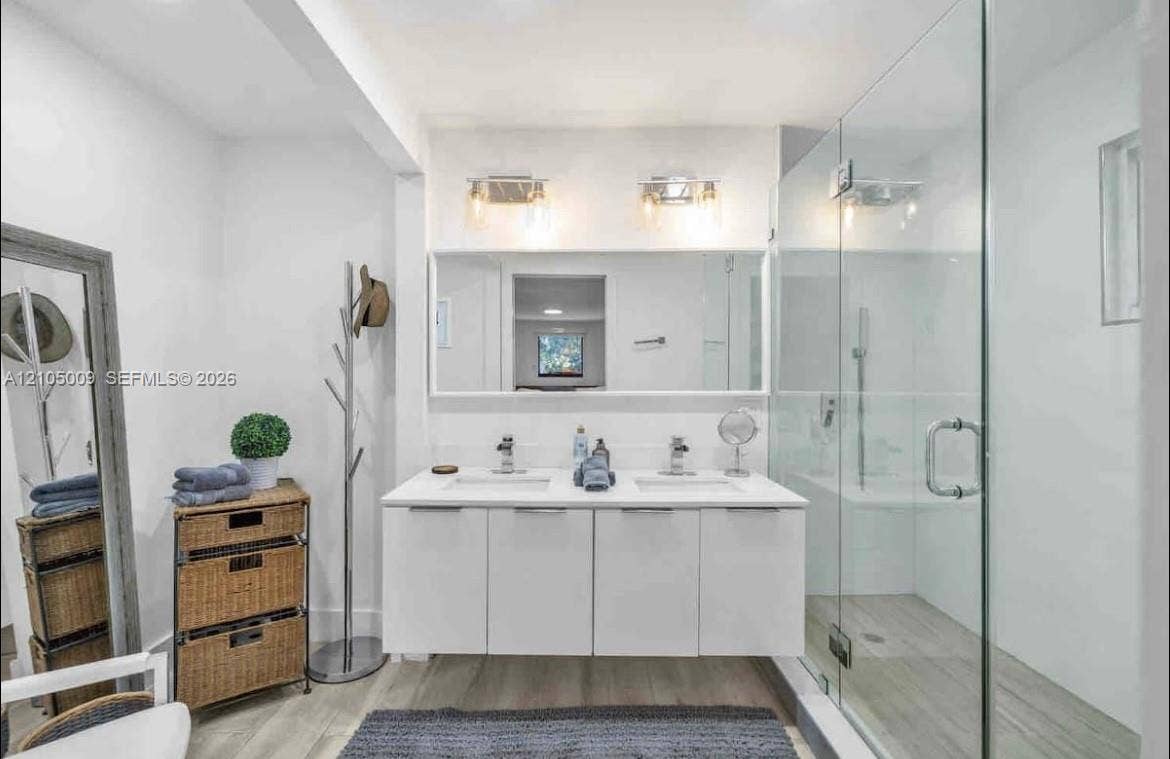 254 NW 51st Street, Miami, Miami, FL 33127 Dual sink vanity with white cabinetry, glass-enclosed shower, light wood-finish flooring, and contemporary wall-mounted light fixtures