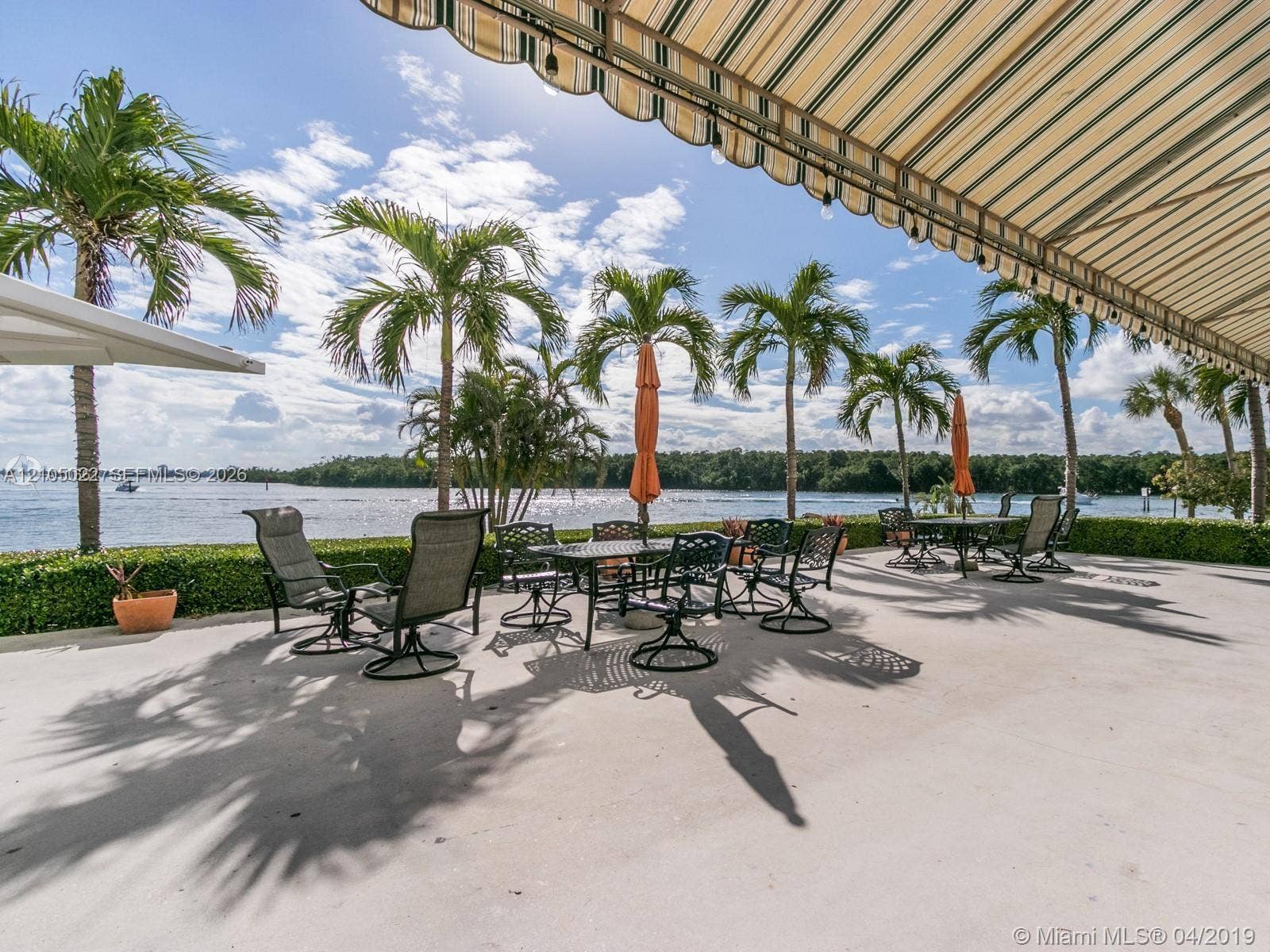 500 Bayview Drive, #1520, Sunny Isles Beach, Sunny Isles Beach, FL 33160 Spacious outdoor patio with water frontage, bordered by a manicured hedge and mature palm trees