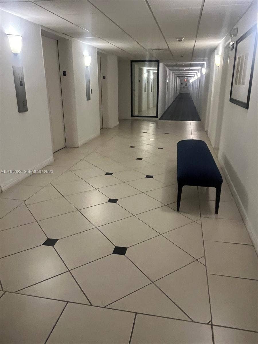 500 Bayview Drive, #1520, Sunny Isles Beach, Sunny Isles Beach, FL 33160 Hallway featuring diagonal tile flooring with black accent squares, wall-mounted sconce lighting, and a full-length mirror