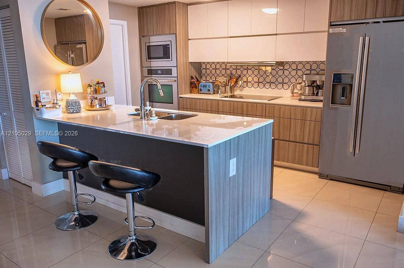 600 NE 27th Street, #1203, Miami, FL 33137 Kitchen featuring a large island with a light-toned countertop, stainless steel appliances, wood-finish cabinetry, built-in oven and microwave, and a patterned tile backsplash