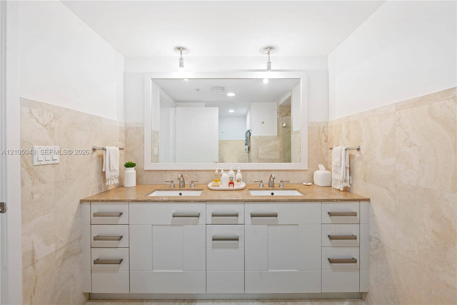 3540 Main Highway, #207, Miami, FL 33133 Dual-sink vanity with stone countertop, large framed wall mirror, stone-tiled shower enclosure with glass door, and wall-mounted metal towel bars