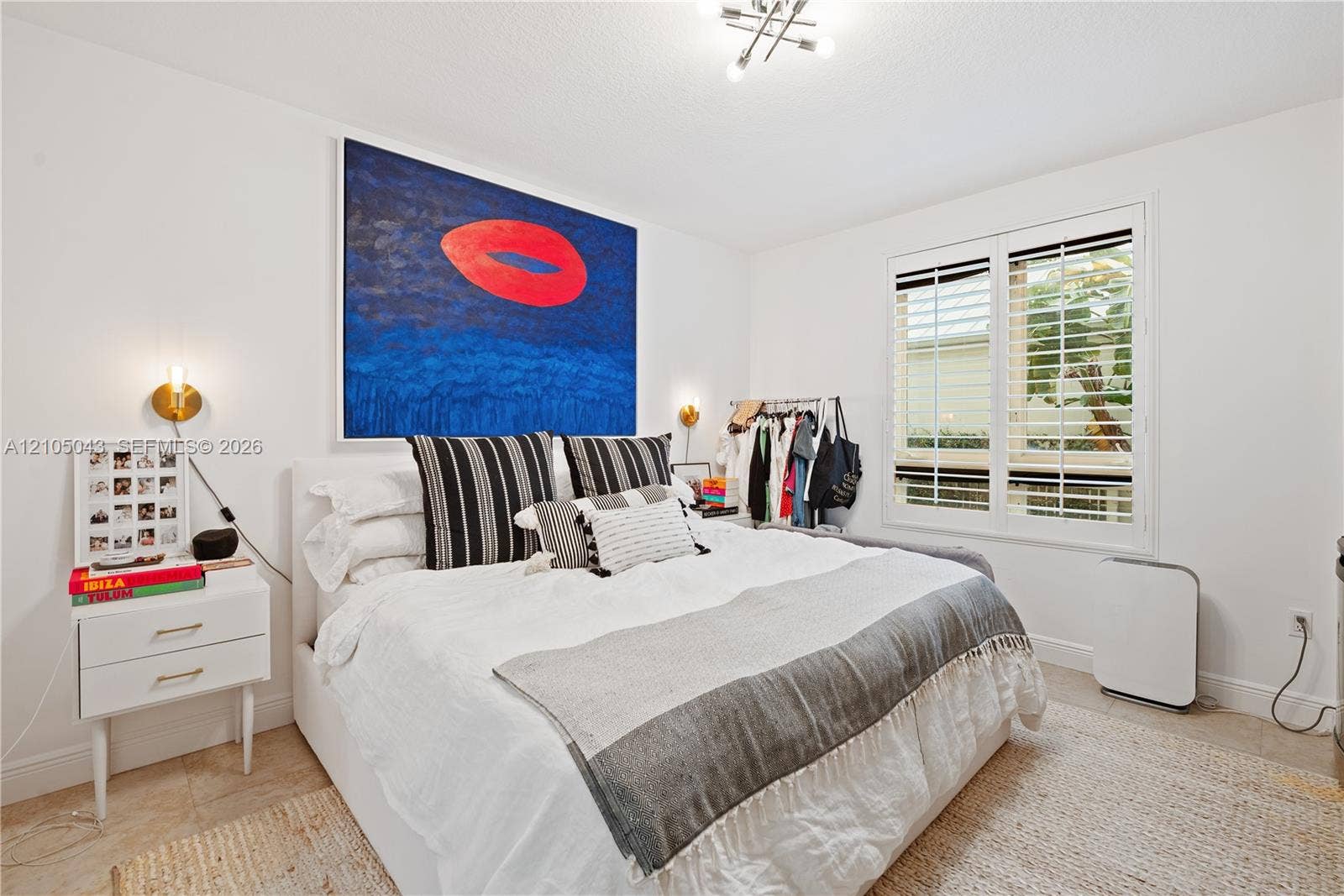 3540 Main Highway, #207, Miami, FL 33133 Bathroom featuring a white vanity cabinet with metallic hardware, light-toned stone countertop, rectangular undermount sink, framed mirror with integrated pendant lighting, and full-height stone wall tile