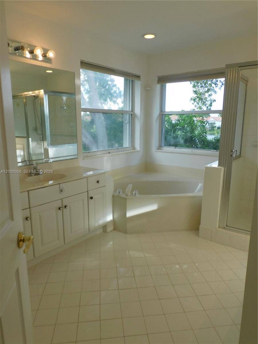 16729 Amber Lake, Weston, FL 33331 Corner soaking tub, tiled flooring, double-hung windows, dual vanitiesy with integrated sink, and enclosed shower
