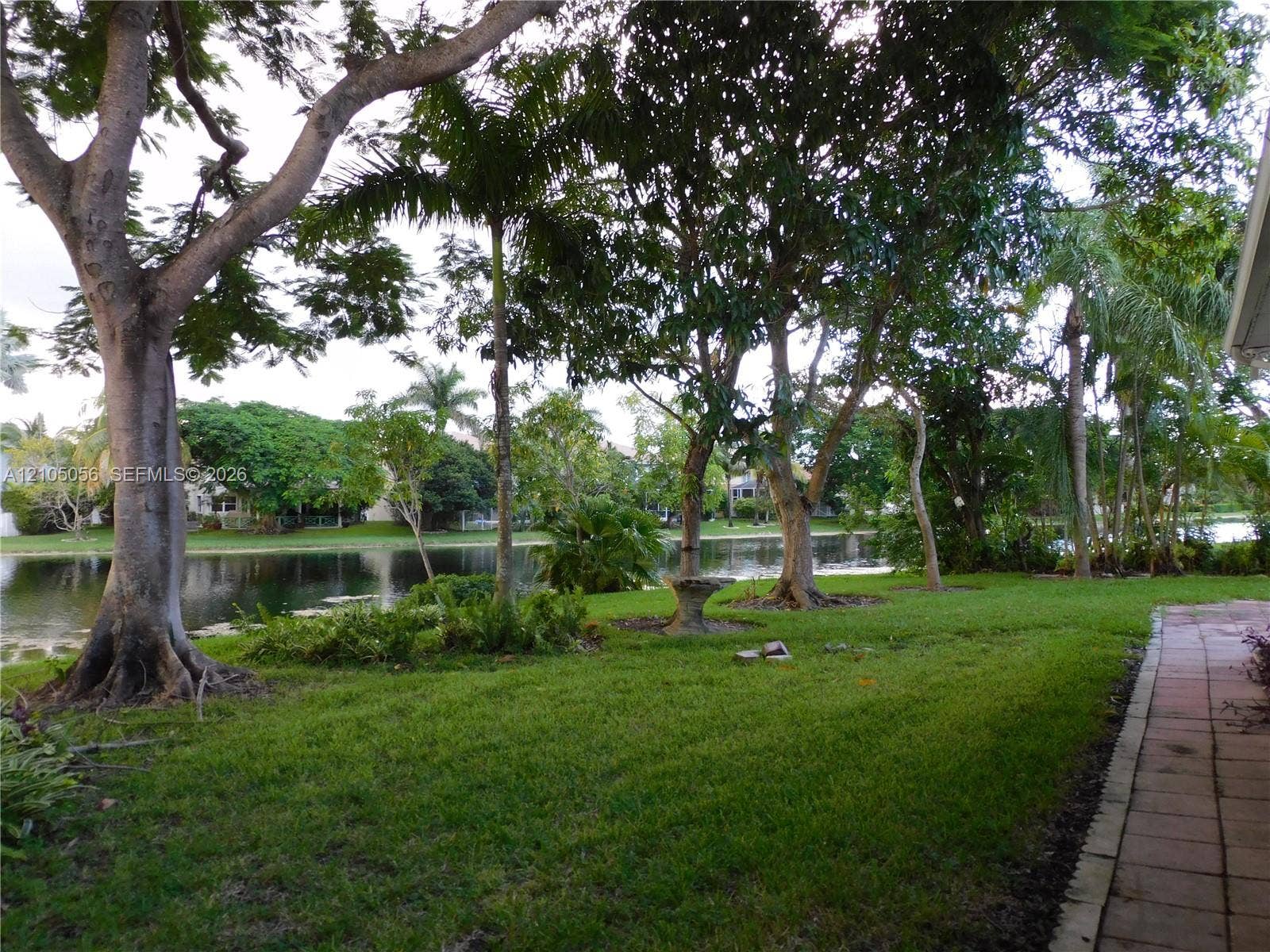 16729 Amber Lake, Weston, FL 33331 Lush green lawn with mature trees, a tranquil waterfront setting, and an adjacent paver pathway