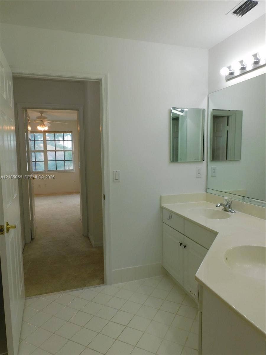 16729 Amber Lake, Weston, FL 33331 White tiled flooring, dual basin vanity, white cabinetry, integrated sinks, wall-mounted light fixture