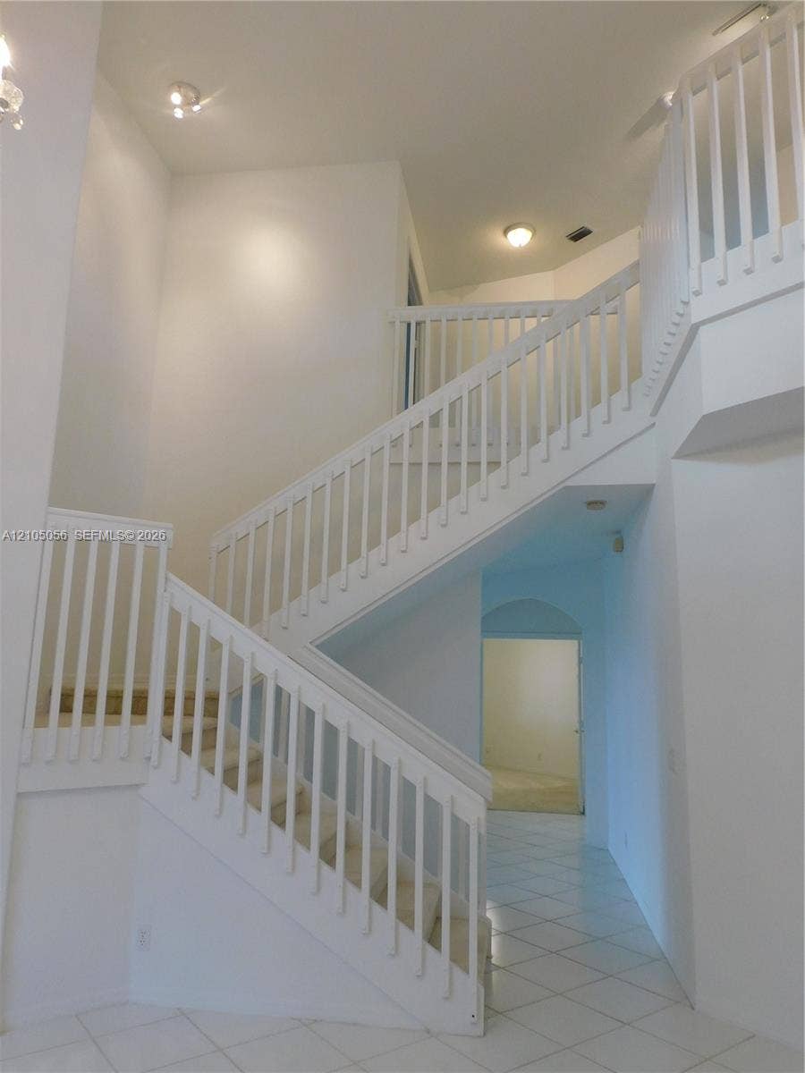 16729 Amber Lake, Weston, FL 33331 Two-story foyer with a bifurcated staircase featuring white railings, carpeted treads, and tiled flooring