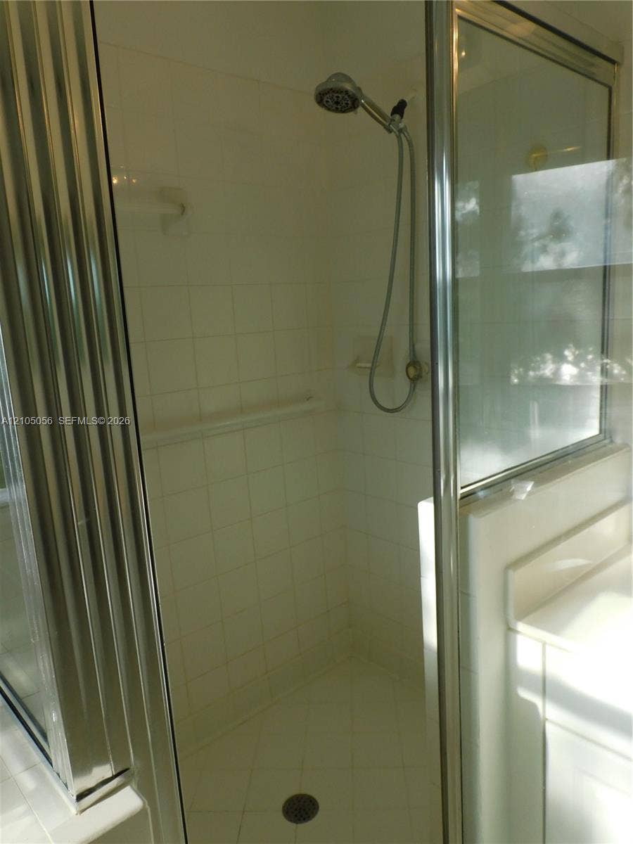 16729 Amber Lake, Weston, FL 33331 Glass-enclosed shower with white tiled walls and floor, featuring a multi-function showerhead and a built-in shower bench