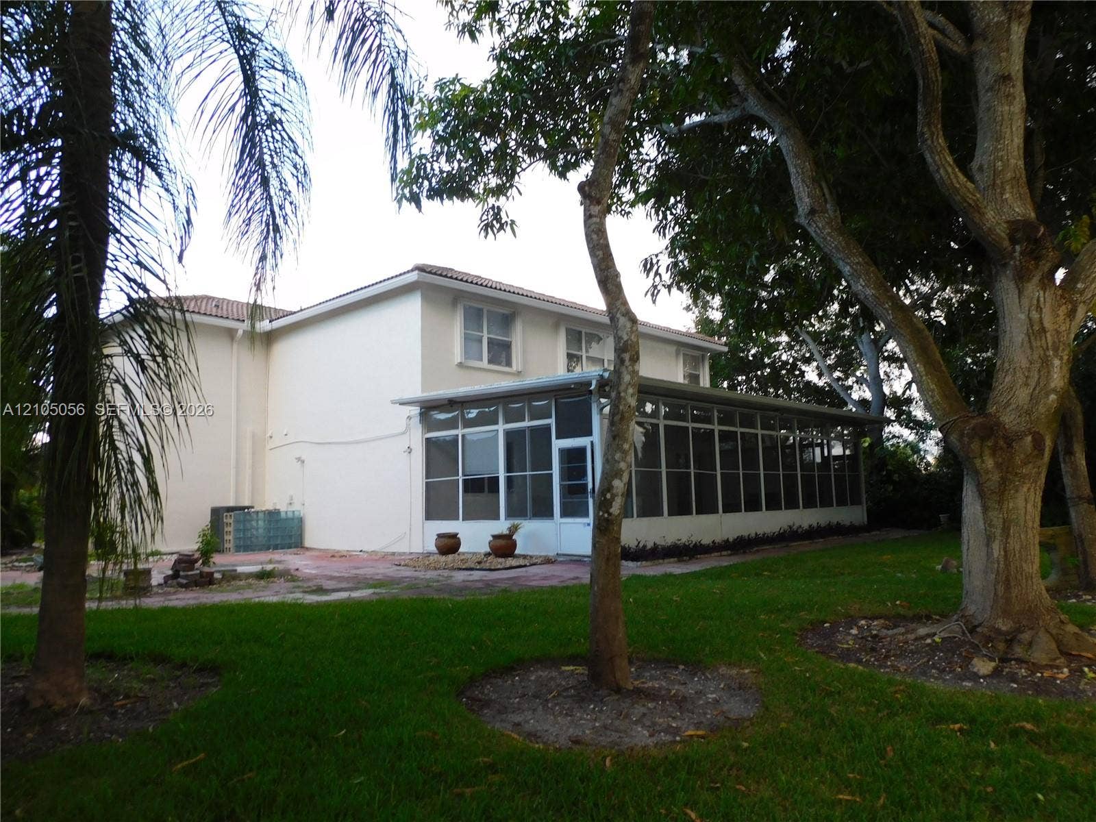 16729 Amber Lake, Weston, FL 33331 Expansive screened patio with white framing, manicured lawn, mature trees, and a two-story exterior