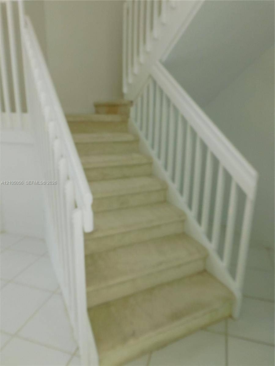 16729 Amber Lake, Weston, FL 33331 Staircase featuring white wood railings and carpeted treads, with tile flooring at the base and leading to upstairs bedrooms and loft.