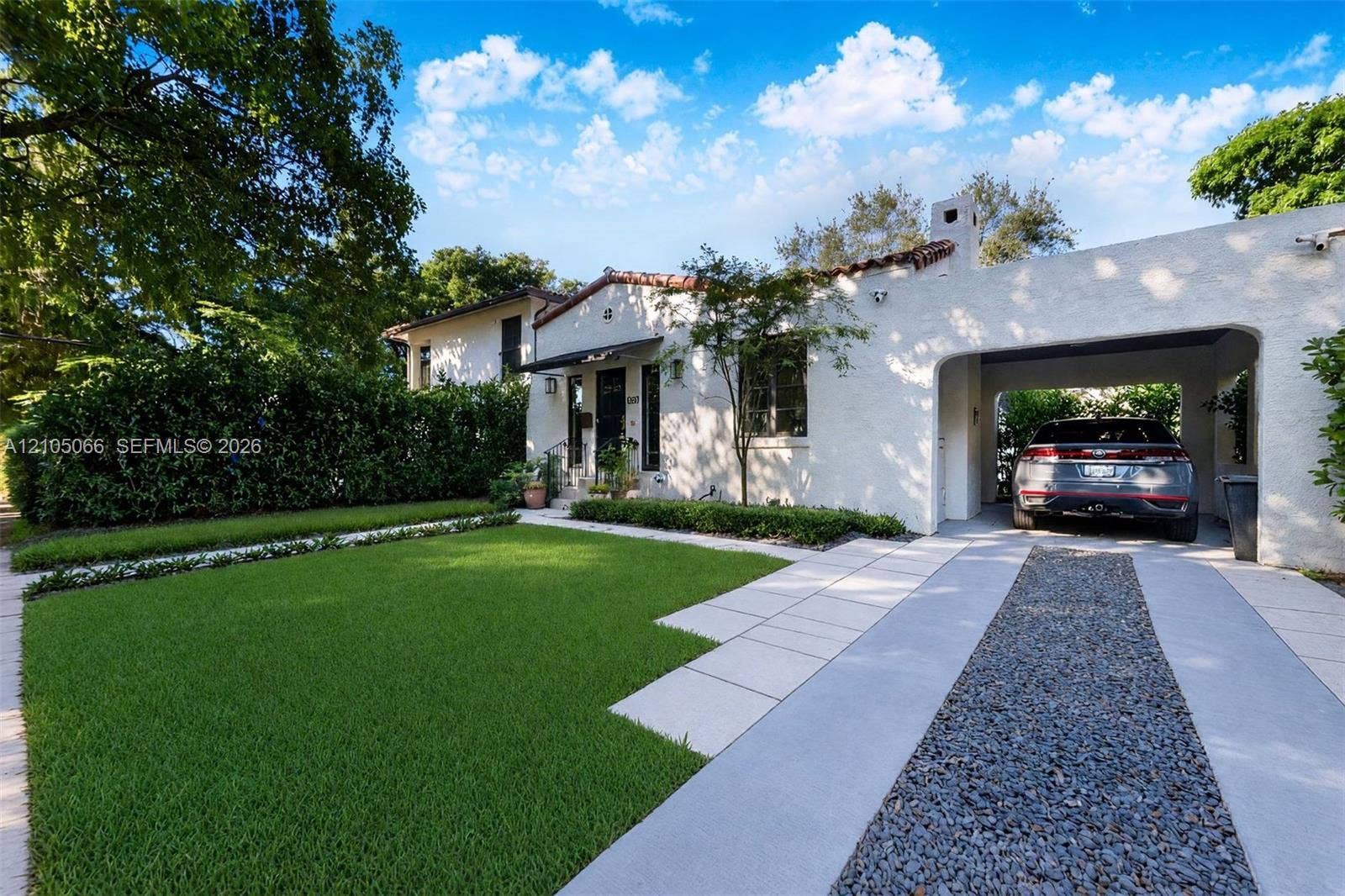 1230 Genoa Street, Coral Gables, Coral Gables, FL 33134 Stucco exterior featuring a tiled roof, arched carport, paved driveway with gravel center inlay, and manicured front lawn