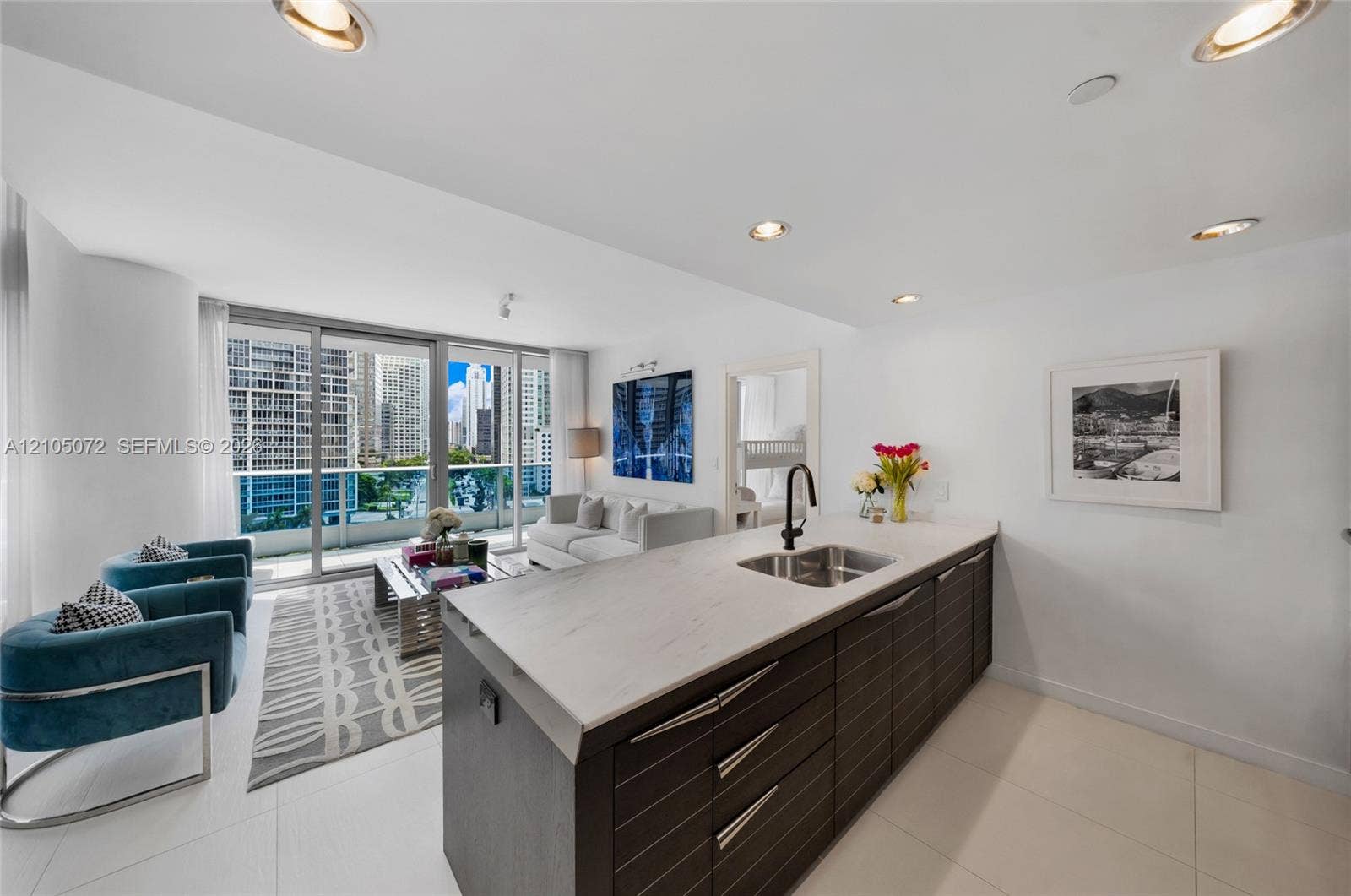 Contemporary kitchen with dark wood-grain cabinetry, Carrara marble island, and adjacent living area.