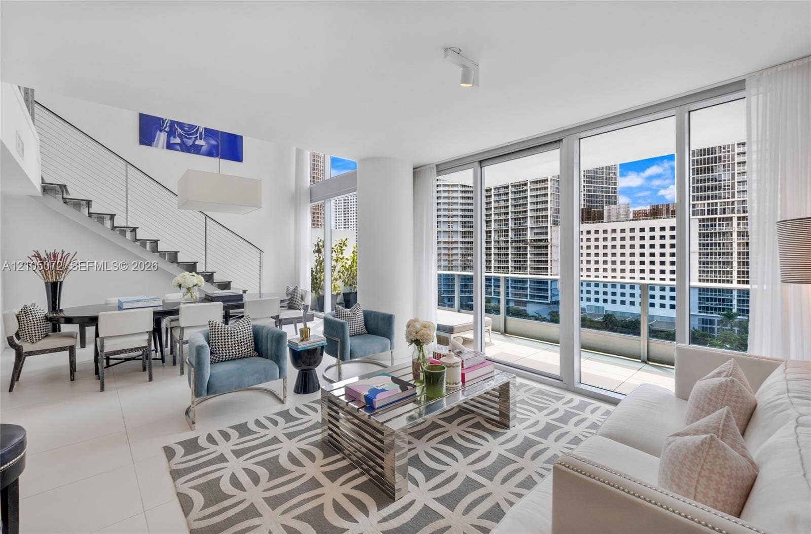 Double-height living room with cable-railed staircase and floor-to-ceiling glass opening to the lower terrace.