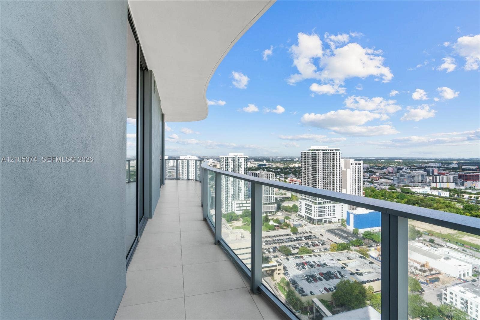 Curved exterior balcony featuring large-format tile flooring, a glass panel railing with a dark metal frame, and sliding glass door access