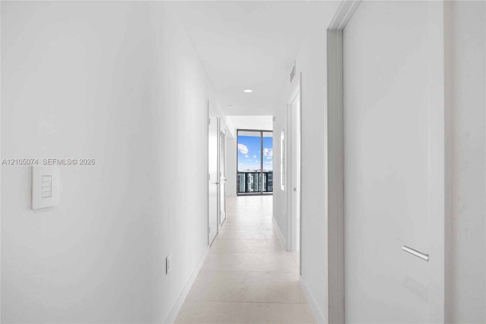 Hallway featuring neutral-toned tile flooring, recessed ceiling lighting, and floor-to-ceiling glass sliding doors