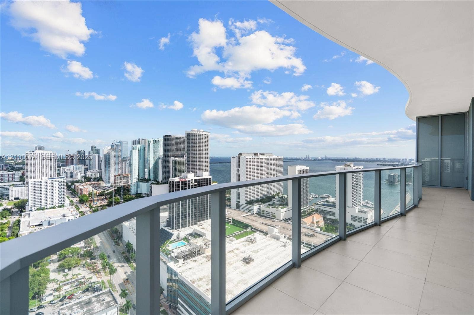 Spacious private balcony with large-format floor tiles and a curved structural design, featuring a glass-panel railing and extensive water and city skyline outlooks