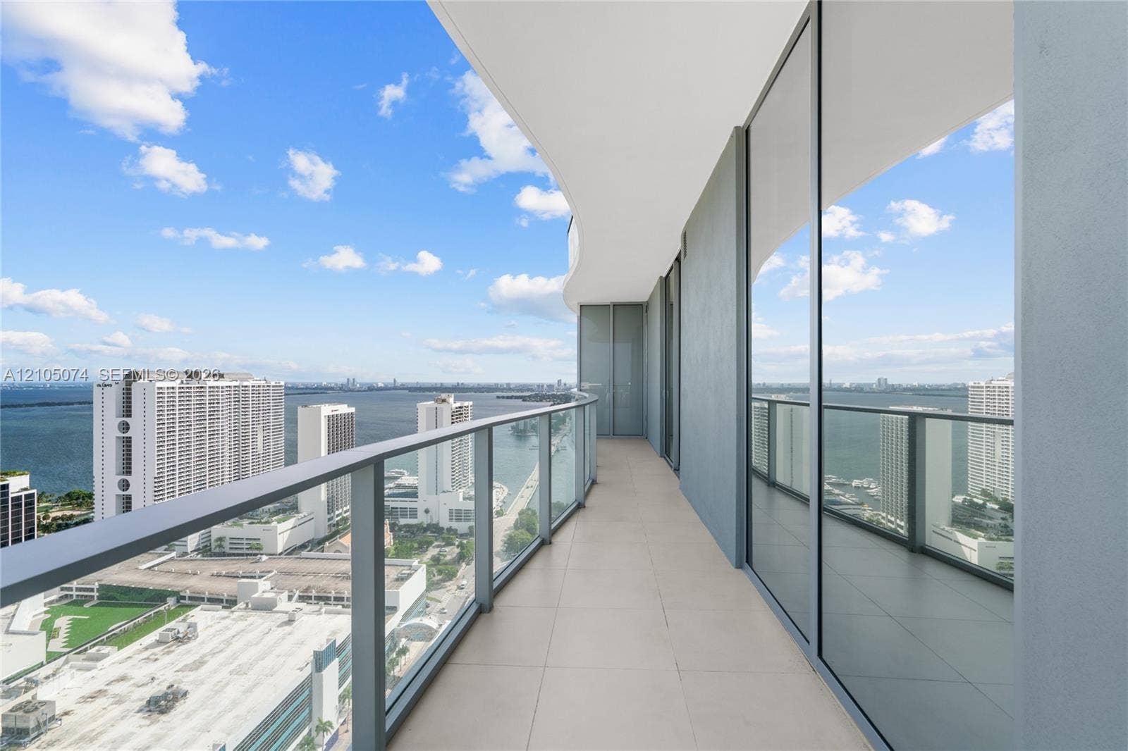 Expansive terrace featuring large-format tile flooring, full-height glass sliding doors, and a sleek glass-paneled railing
