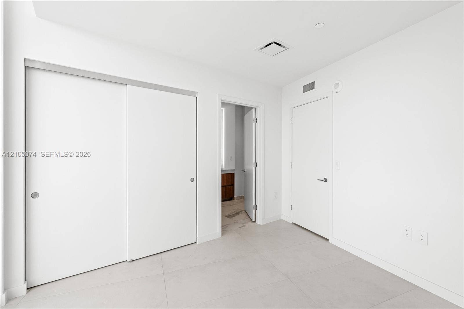 Neutral-toned large-format tile flooring, sliding closet doors, and solid-core swing door with brushed nickel hardware