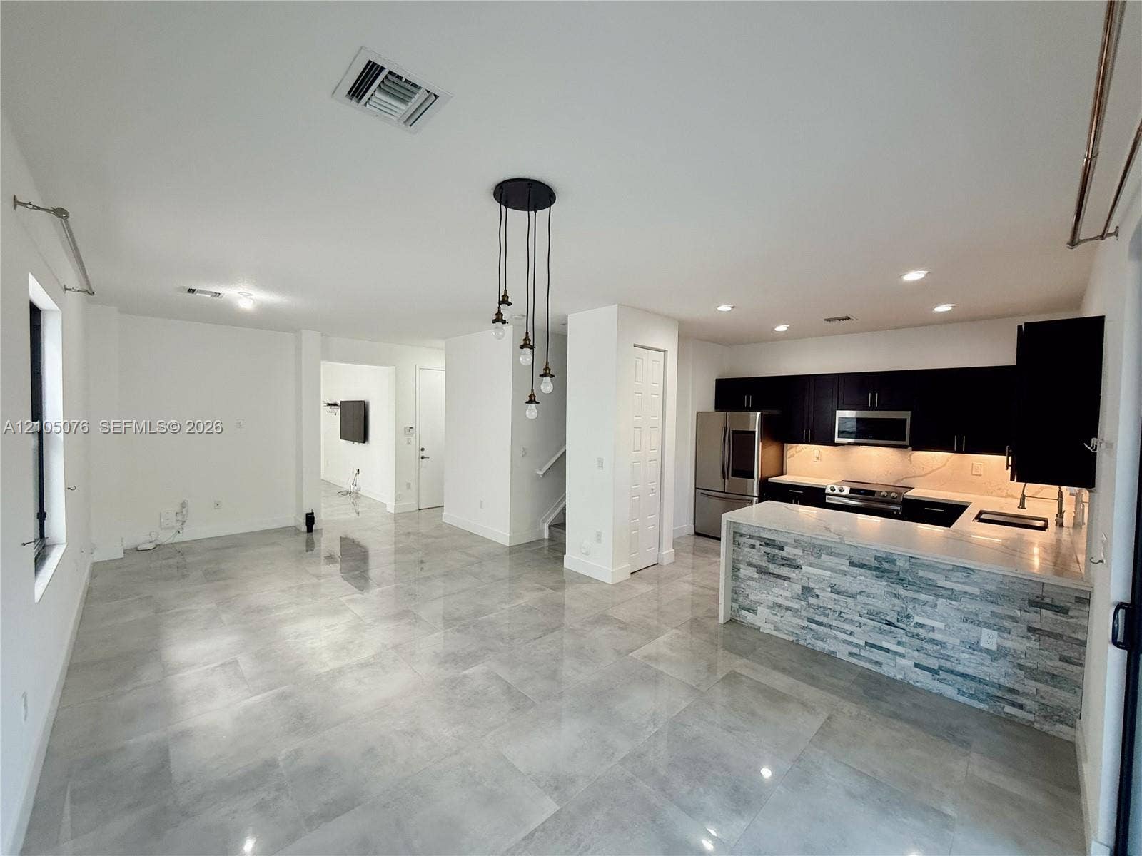 717 NE 191st Street, Miami, FL 33179 Open-concept area featuring oversized neutral tile flooring, kitchen with dark cabinetry, stone-veneer breakfast bar, and industrial-style pendant lighting