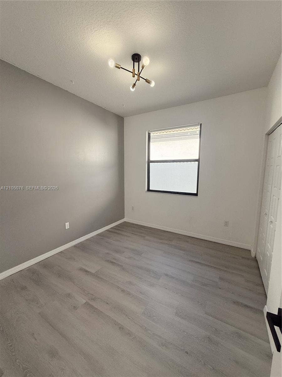 717 NE 191st Street, Miami, FL 33179 Interior room featuring wood-finish flooring, a multi-arm modern light fixture, a single window, and dual-panel closet doors