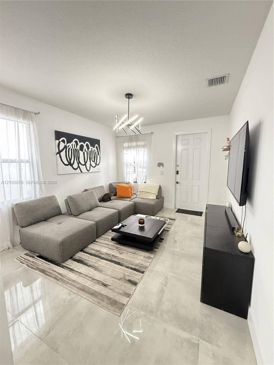 717 NE 191st Street, Miami, FL 33179 Living area featuring large-format light-toned tile flooring, multi-paned windows, and a contemporary geometric chandelier