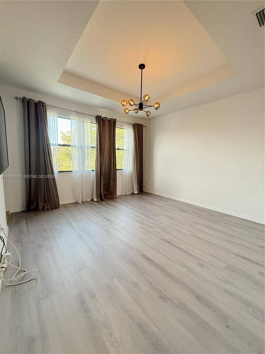 717 NE 191st Street, Miami, FL 33179 Tray ceiling with central multi-globe chandelier, wood-finish flooring, and expansive windows