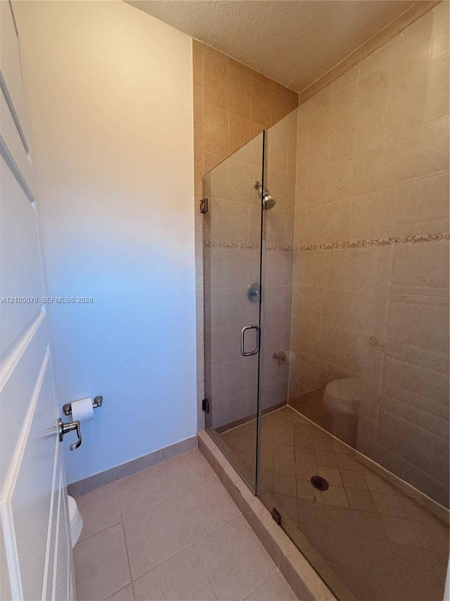 717 NE 191st Street, Miami, FL 33179 Walk-in shower enclosure with frameless glass door, neutral ceramic tile surround, integrated decorative tile inlay, and chrome finish hardware
