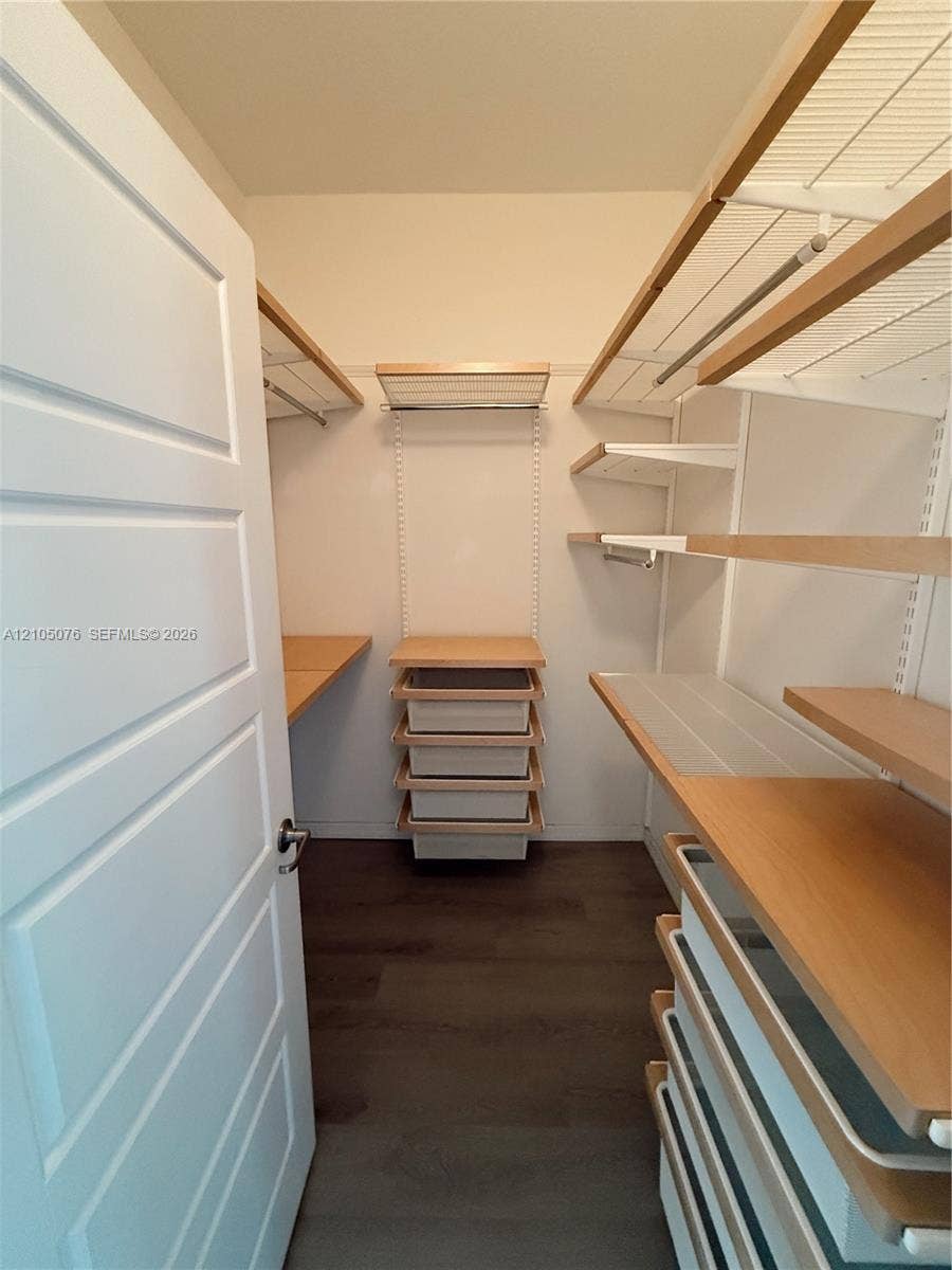 717 NE 191st Street, Miami, FL 33179 Walk-in closet featuring multi-level wood-finish shelving, integrated pull-out drawers, white metal support tracks, and dark wood-finish flooring