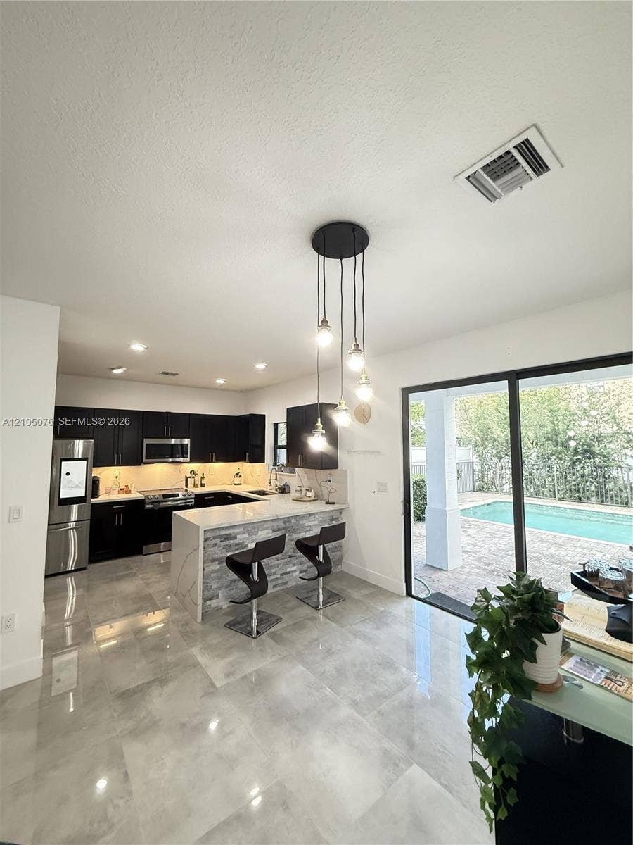 717 NE 191st Street, Miami, FL 33179 Kitchen featuring dark cabinetry, stone-finish countertops, stainless steel appliances, a stacked-stone kitchen island, and polished tile flooring