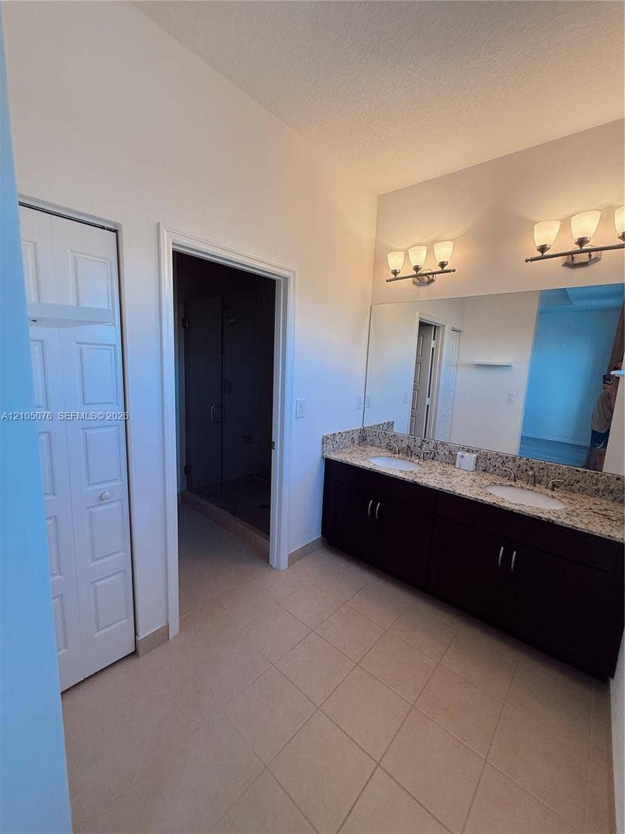 717 NE 191st Street, Miami, FL 33179 Bathroom featuring a dual-sink vanity with stone-finish countertop, dark cabinetry, large wall-mounted mirror, and tile flooring