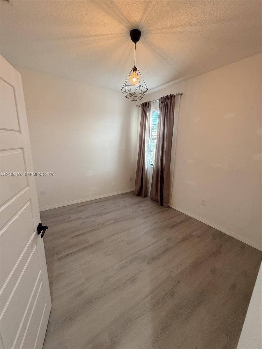 717 NE 191st Street, Miami, FL 33179 Room featuring wood-finish flooring, a geometric pendant light fixture, and a single-panel interior door with matte black hardware
