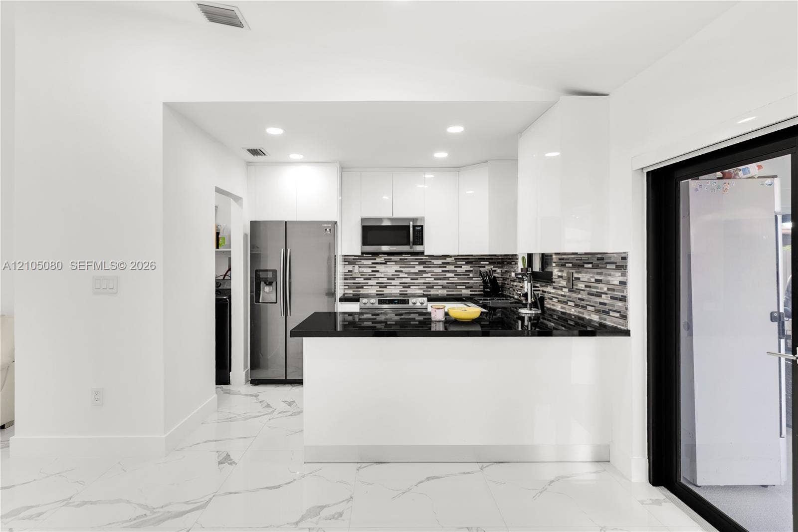 9755 SW 148th Court, Miami, FL 33196 Kitchen featuring white flat-panel cabinetry, black stone countertops, multi-toned mosaic tile backsplash, stainless steel built-in appliances, and large-format tile flooring with veining detail