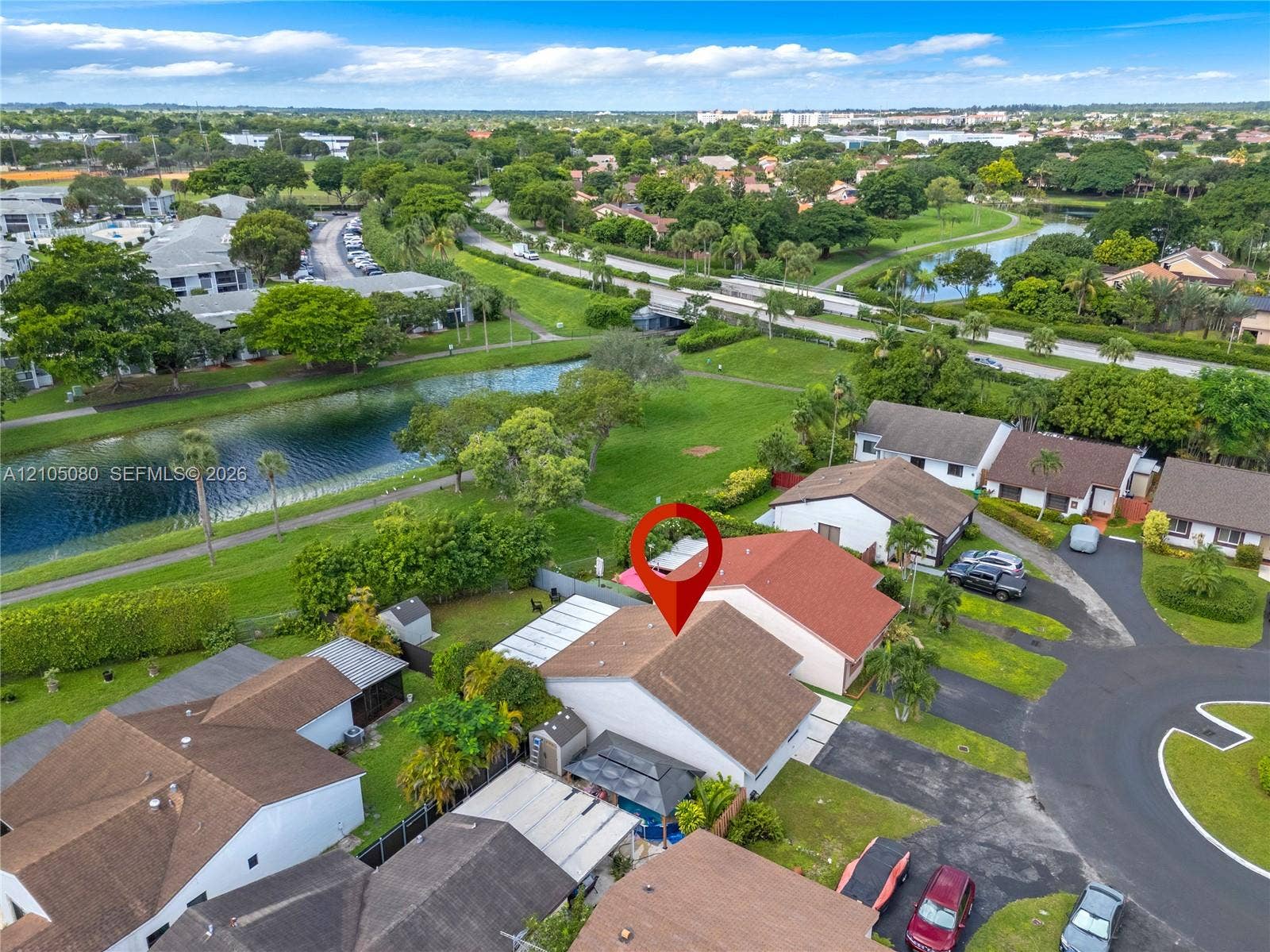 9755 SW 148th Court, Miami, FL 33196 Aerial perspective featuring a residential property with a shingle roof, paved driveway, and rear patio cover, situated in a community with expansive green space and water frontage