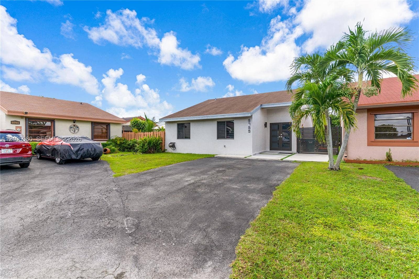 9755 SW 148th Court, Miami, FL 33196 Single-story residence featuring a light-toned exterior, dark-framed double front entry doors, asphalt-paved driveway, and mature landscaping