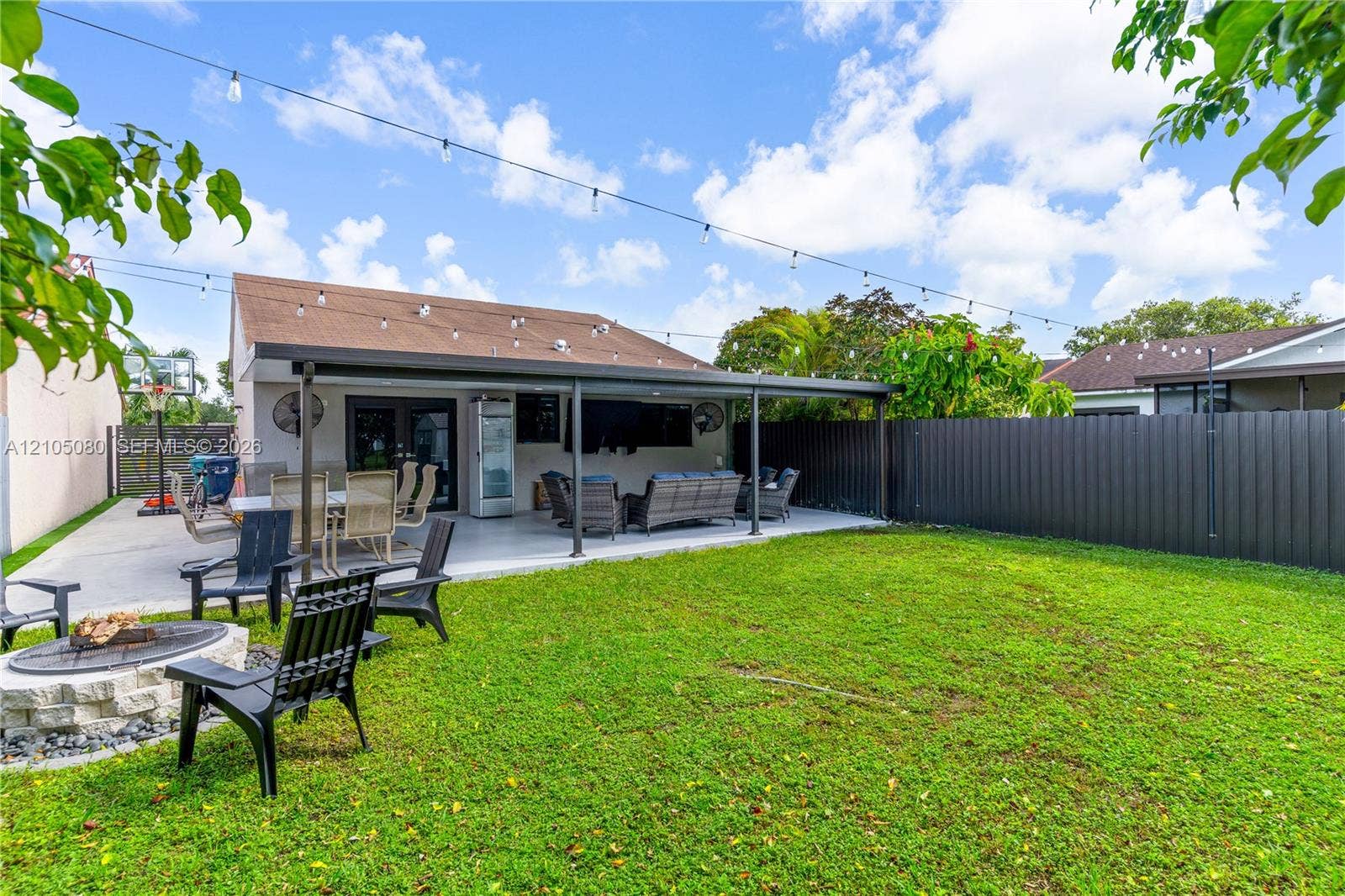 9755 SW 148th Court, Miami, FL 33196 Backyard featuring a covered concrete patio, stone-finish fire pit, string lighting, and privacy fencing