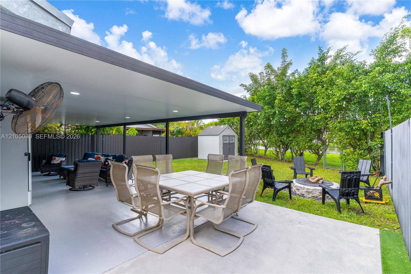 9755 SW 148th Court, Miami, FL 33196 Covered outdoor patio featuring recessed lighting and a wall-mounted fan, stone-bordered fire pit, and enclosed backyard with perimeter fencing