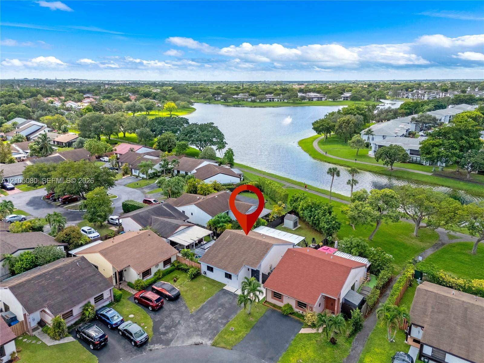 9755 SW 148th Court, Miami, FL 33196 Aerial perspective featuring a residential lot with a paved driveway, shingled roofing, and a coastal landscape including a proximate lake and mature greenery