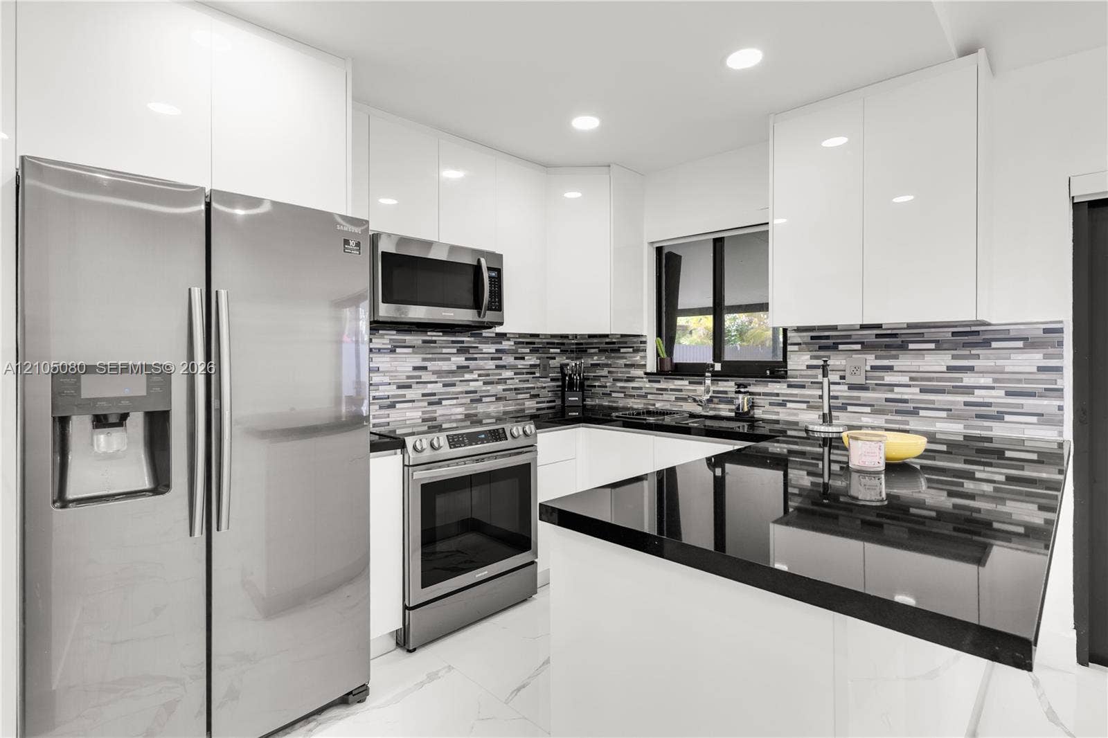 9755 SW 148th Court, Miami, FL 33196 Kitchen featuring high-gloss white cabinetry, dark stone-finish countertops, stainless steel appliances, multi-toned mosaic tile backsplash, and large-format tile flooring