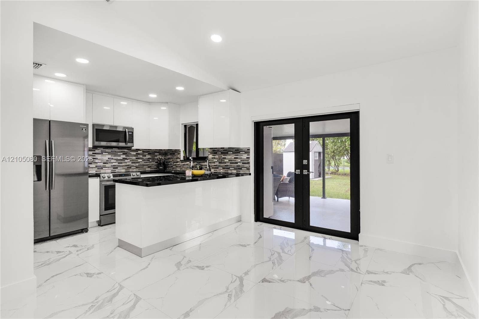 9755 SW 148th Court, Miami, FL 33196 Kitchen featuring high-gloss white cabinetry, stone-finish countertops, stainless steel appliances, a multi-tonal backsplash, and large-format porcelain tile flooring with a marbled aesthetic