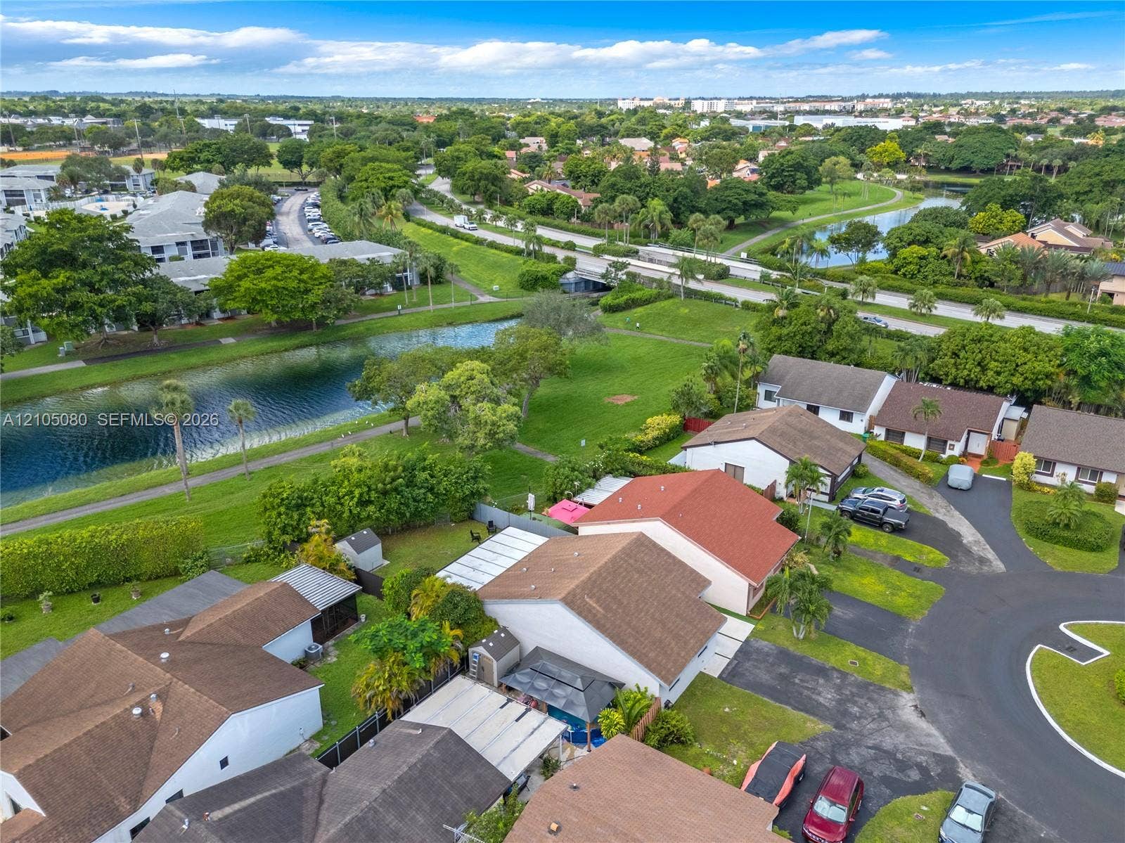 9755 SW 148th Court, Miami, FL 33196 Aerial perspective of a suburban neighborhood featuring a canal, mature trees, multi-pitched shingled roofing, and paved cul-de-sac streets