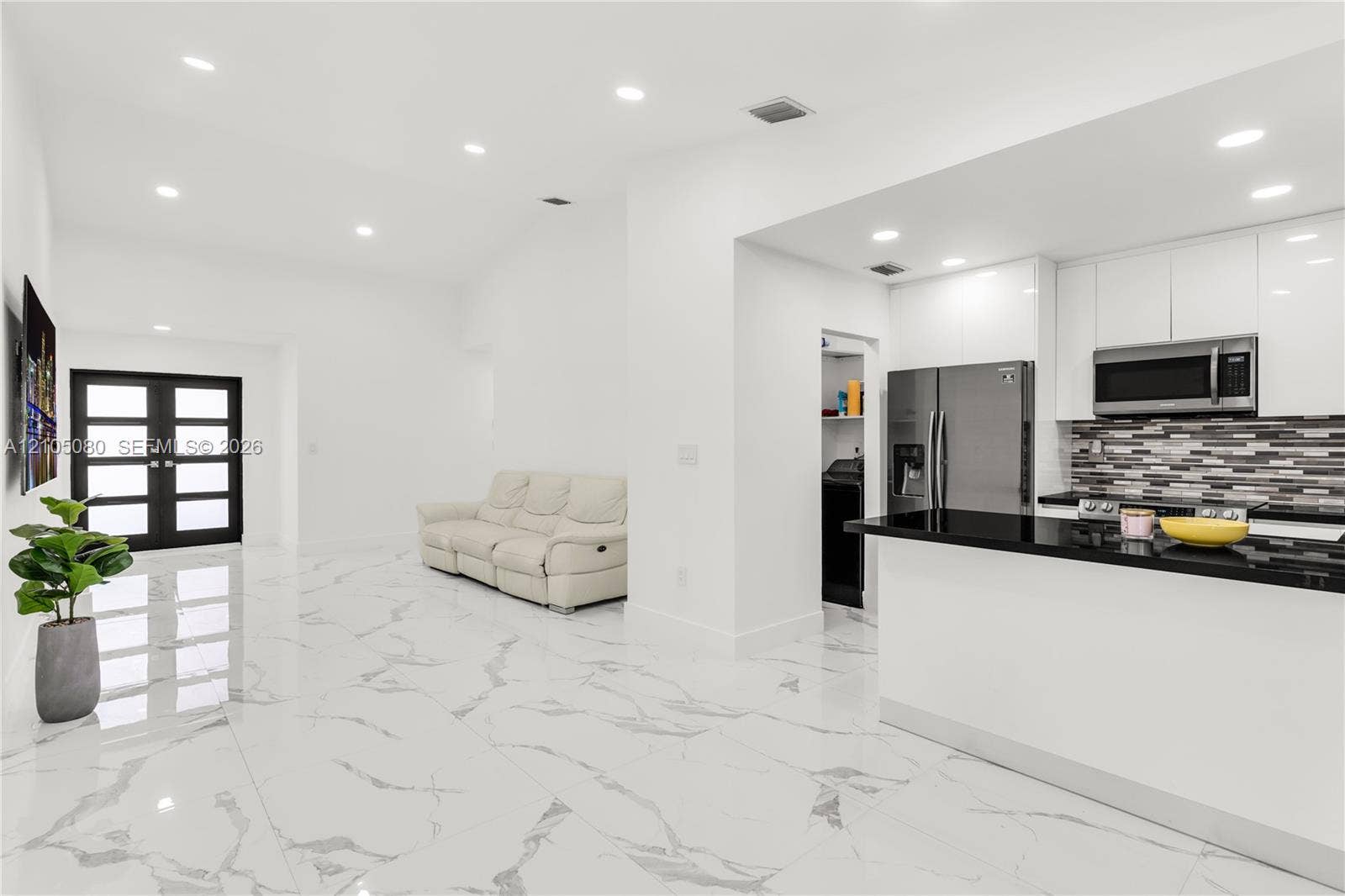 9755 SW 148th Court, Miami, FL 33196 Interior space featuring high-gloss, large-format tile flooring, recessed ceiling lighting, a kitchen with white cabinetry and dark stone-surface countertops, a multi-pane glass-panel entry door, and a decorative tile backsplash