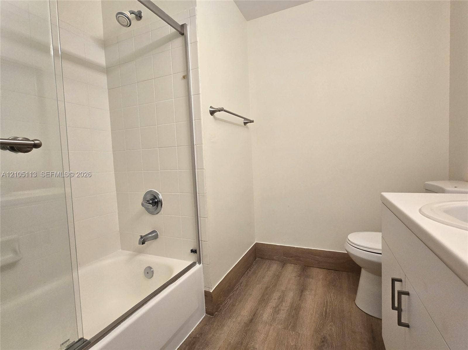 2020 Pompeii Court, Weston, Weston, FL 33327 Bathtub with glass enclosure and shower head, white tiled shower surround, wood-finish flooring, white vanity with integrated sink, and white toilet