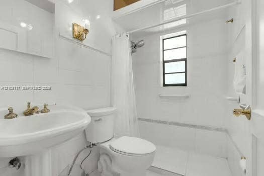 6851 SW 32nd Street, Miami, FL 33155 Bathroom featuring a pedestal sink with brass-toned hardware, white wall tile, a combination tub and shower enclosure with a window, and brass-toned sconce lighting
