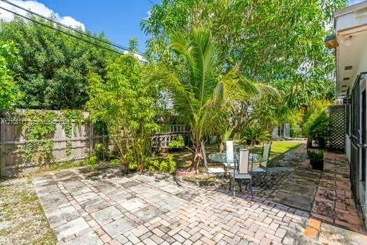 6851 SW 32nd Street, Miami, FL 33155 Private backyard featuring a paved stone patio, perimeter wood fencing, established tropical landscaping, and mature trees